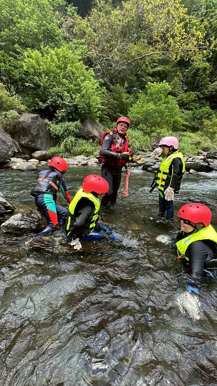 孩子們戴安全帽、穿救生衣,在溪水裡跟著教練練習