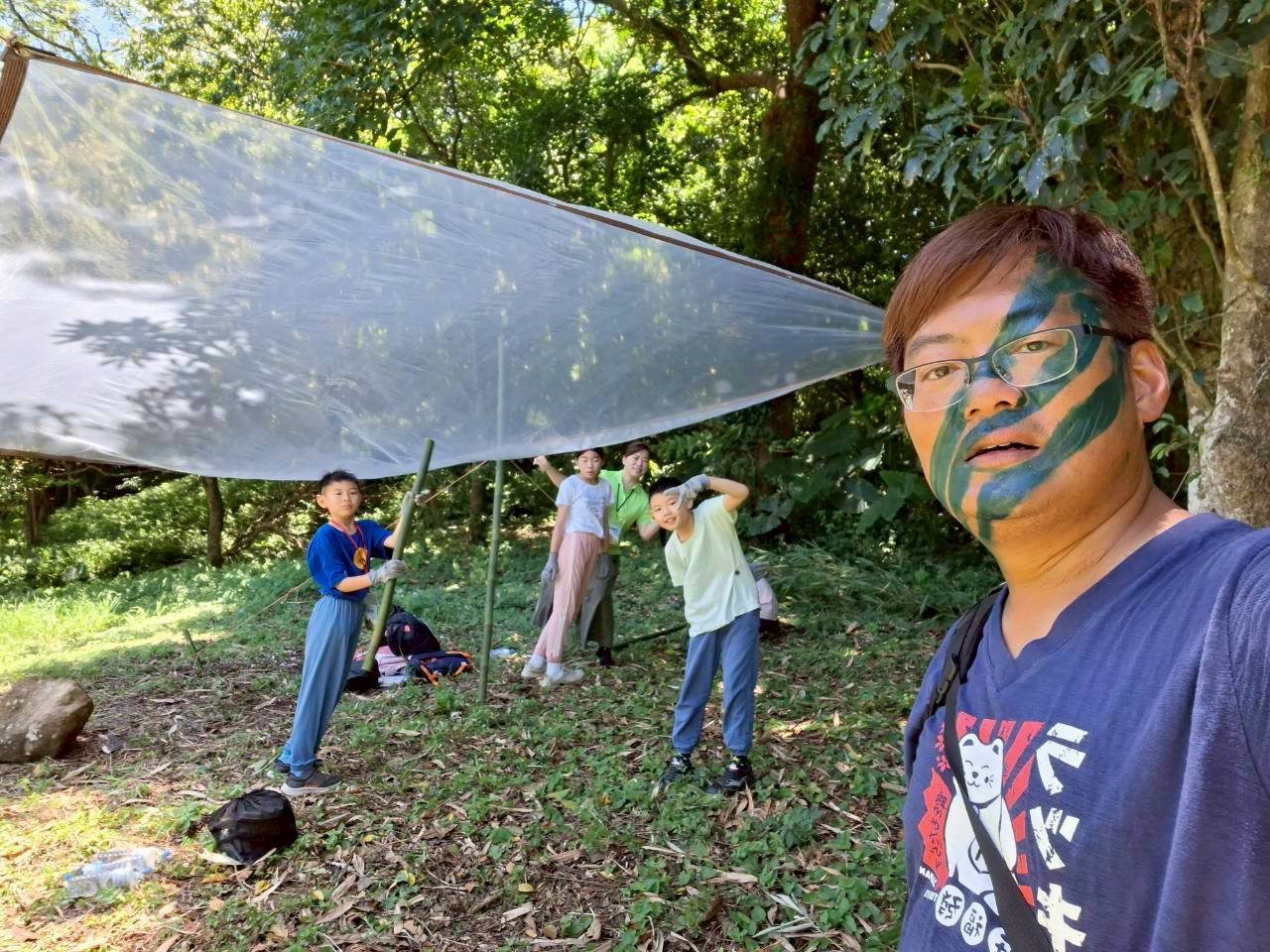 孩子們在樹林裡用竹竿把塑膠布撐成遮雨棚