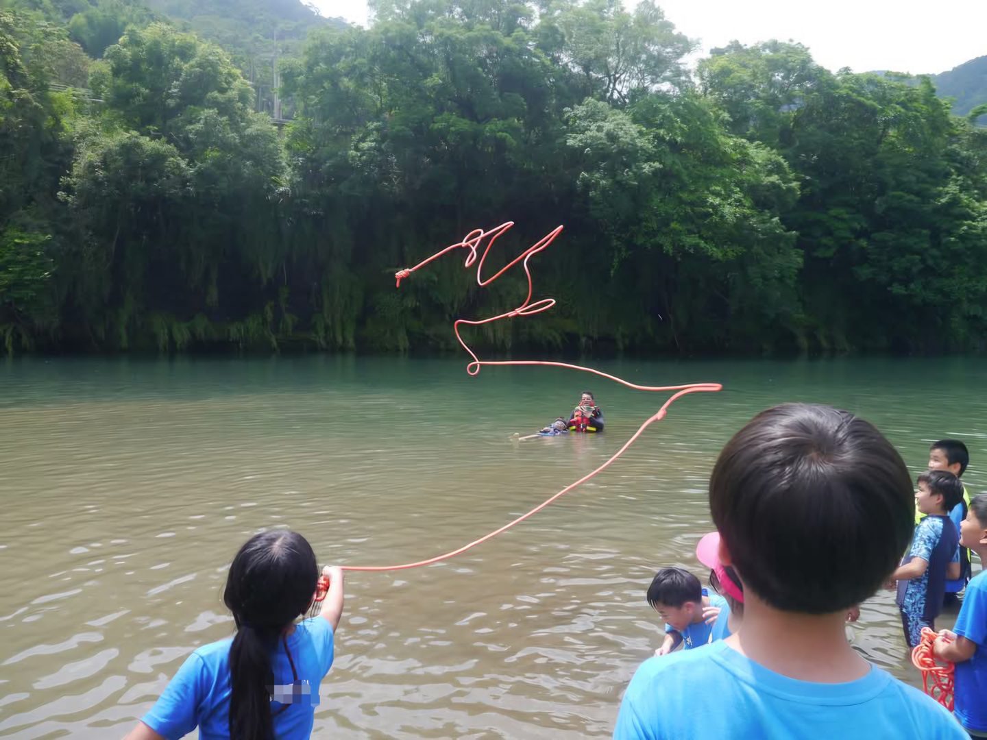 孩子站在溪邊淺水裡,把救生拋繩甩向河中央