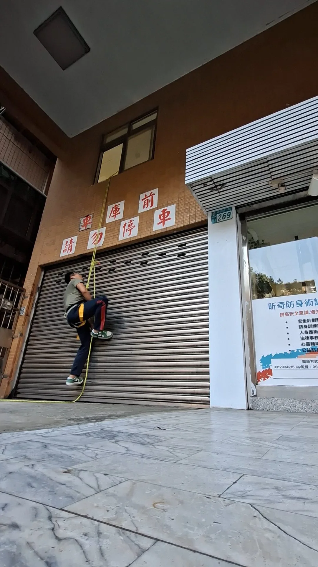 中興路一段 269 號店門口，有人拉著繩索踩著鐵捲門往上爬