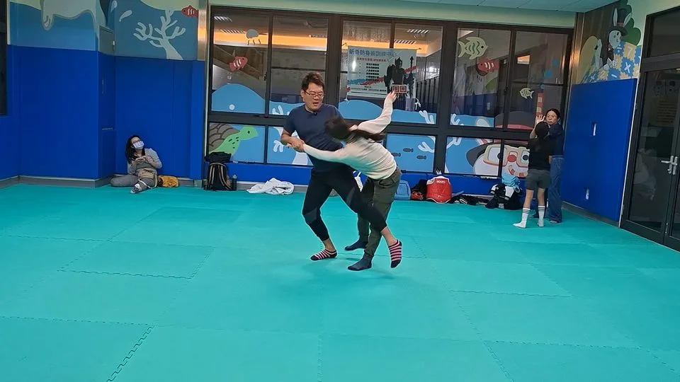 教練示範把女學員往側邊帶倒，旁邊有學員在看